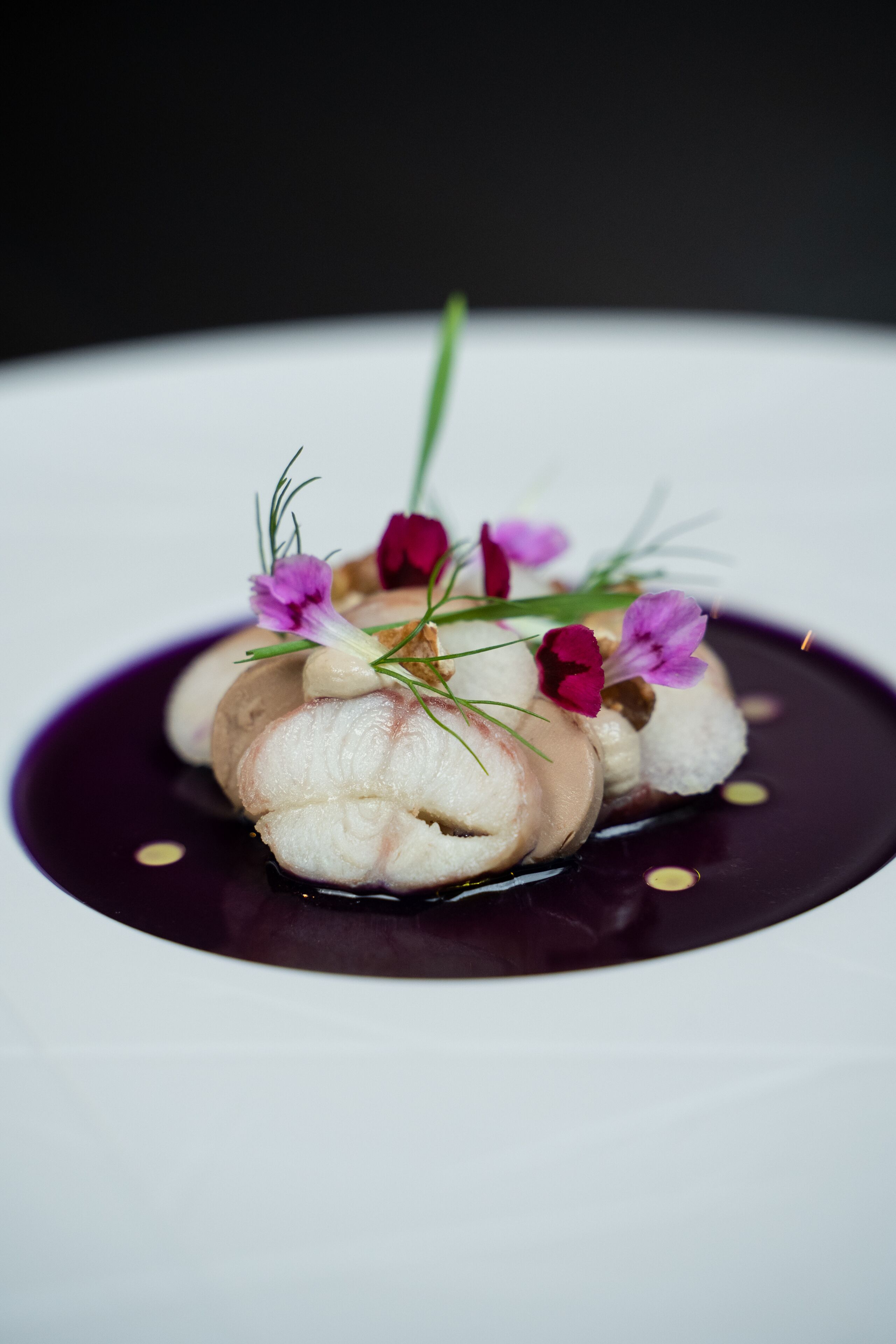Un dessert nappé d’une sauce foncée et agrémenté de quelques décorations, le tout présenté sur une assiette blanche.