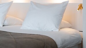 Un dormitorio moderno con cabecera de mármol, ropa de cama blanca y una lámpara de noche.