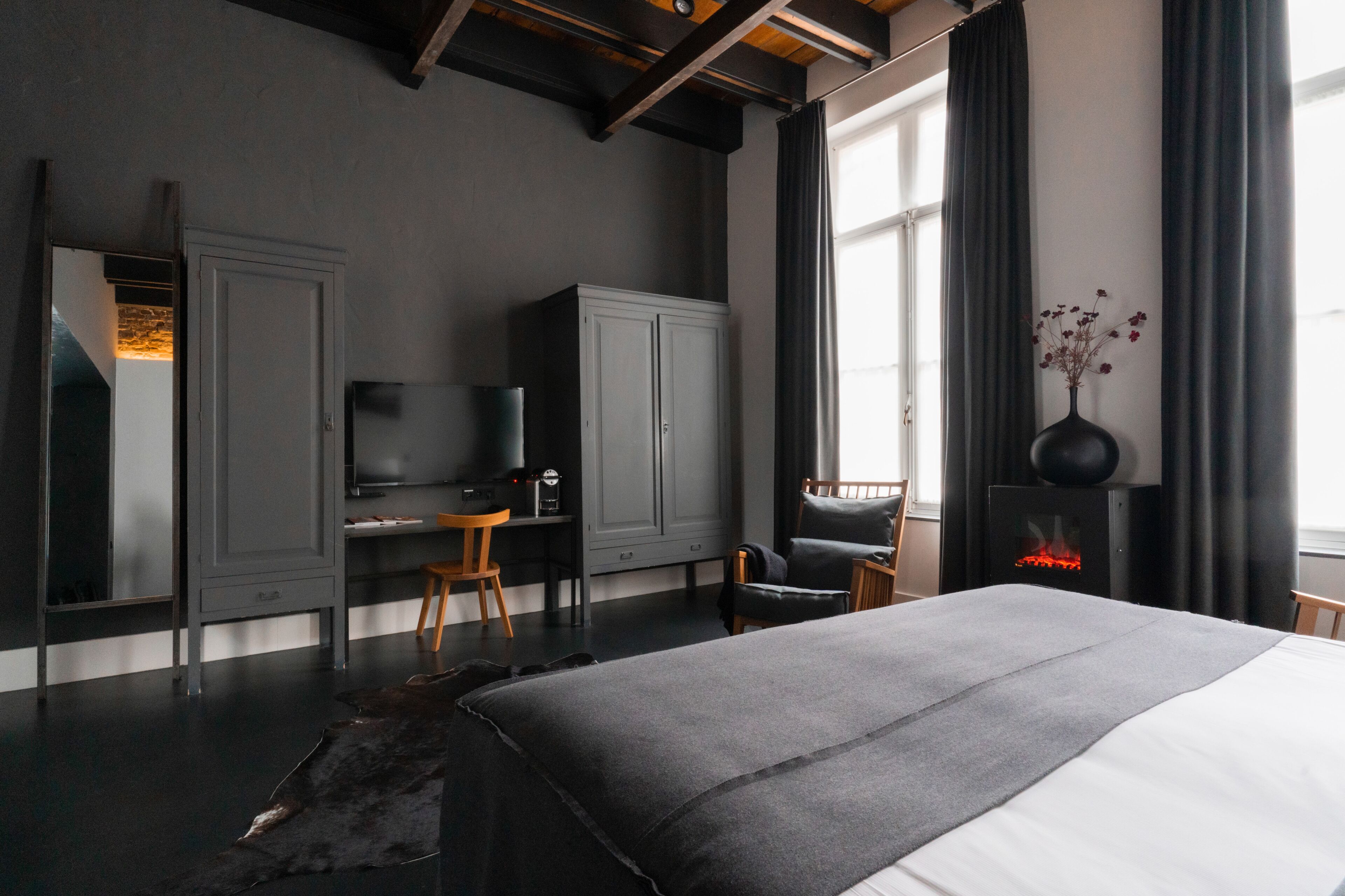 A modern bedroom with a large bed, a desk, a television, and a fireplace.