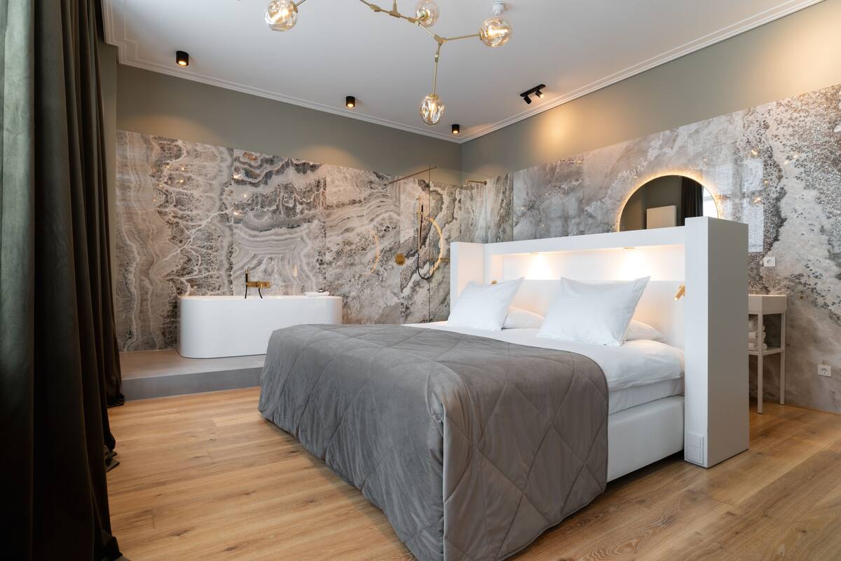 Ein modernes Schlafzimmer mit einem großen Bett, einer integrierten Badewanne und einer Marmorwand.