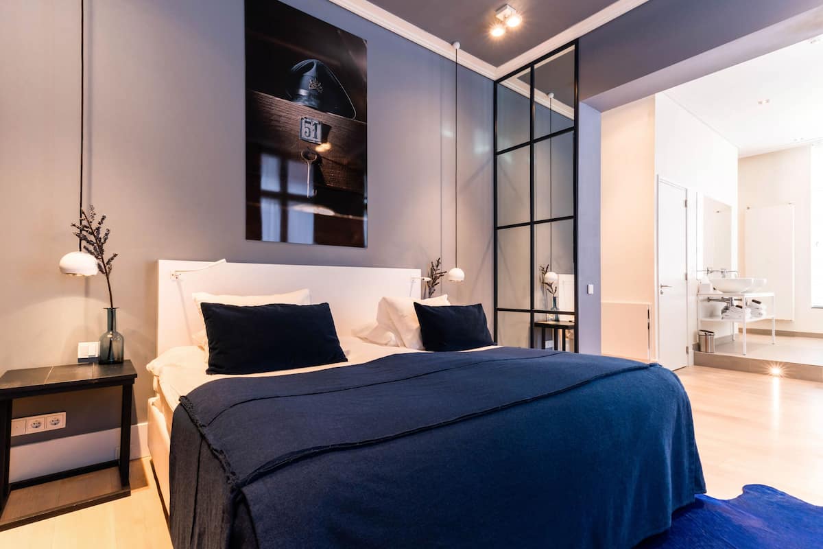 Ein modernes Schlafzimmer mit einem großen Bett, einem Nachttisch, einer an der Wand befestigten Uhr und einer Schiebetür zu einem Badezimmer.