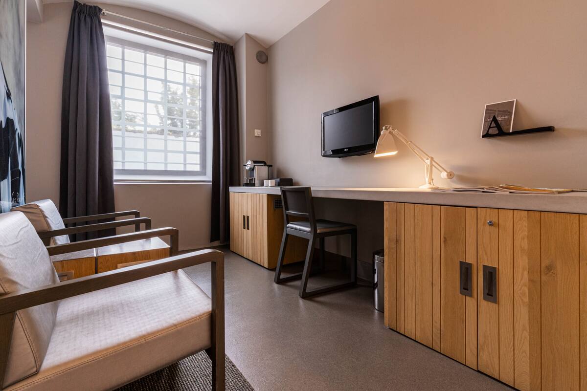 Ein Hotelzimmer mit Bett, Schreibtisch, Stuhl, Fernseher und einem Fenster mit Vorhängen.