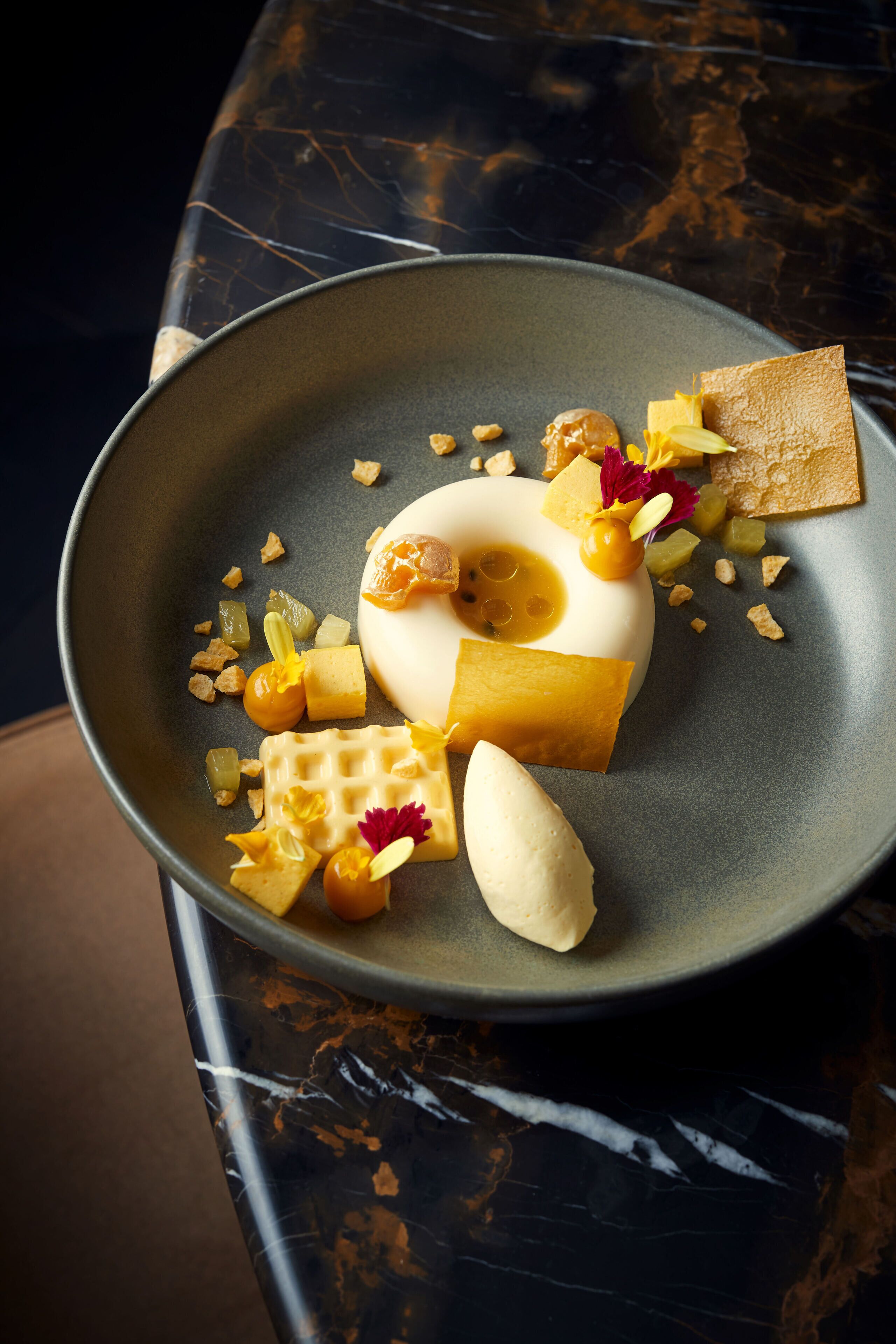 A dessert plate with various sweet items and garnishes on a dark marble table.