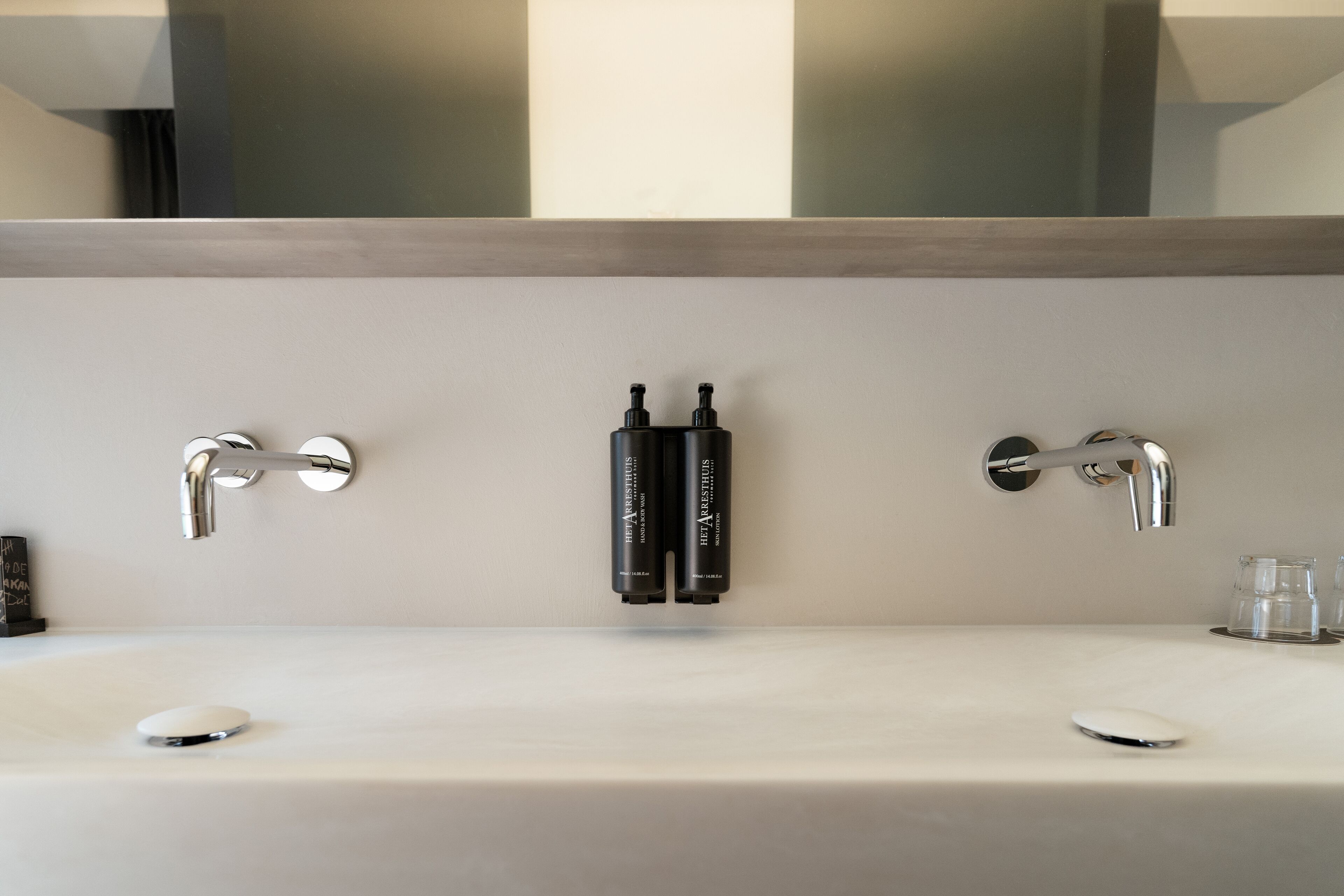 Un baño moderno con lavamanos doble, dos grifos y un espejo encima.