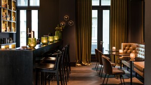 Zona de bar moderna con una barra larga, varios taburetes y un área de estar con sofá y sillones.