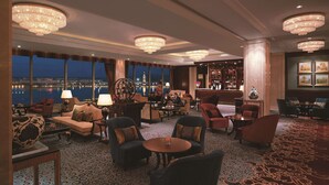 Ein großzügiger Loungebereich mit verschiedenen Sitzgelegenheiten, einer Bar und großen Fenstern mit Blick auf die Stadt.