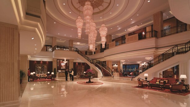 Eine geräumige Lobby mit einer imposanten Treppe, verschiedenen Sitzbereichen und einer großen Chandelier.