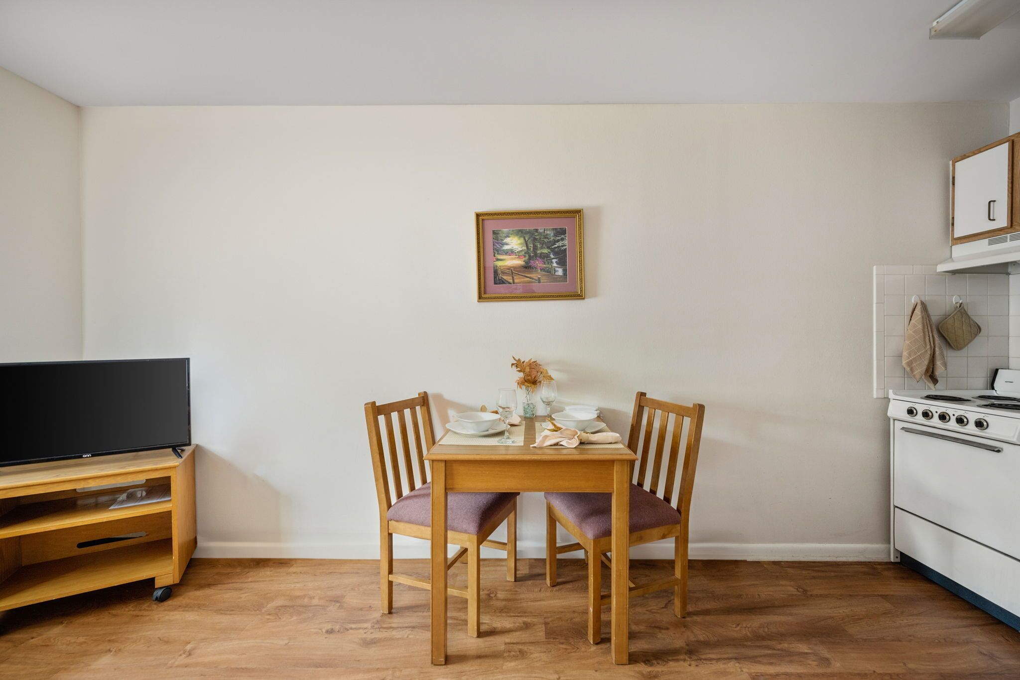 A compact kitchen with a dining table, chairs, a TV, and a stove.