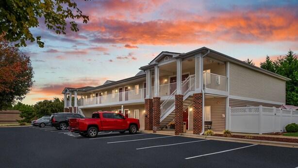 A motel with a two-story structure, a covered front porch, and a parking lot with several vehicles. - Affordable Suites Hickory/Conover (Conover)