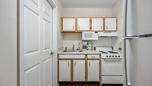 A compact kitchen with white cabinets, a microwave, a stove, and a refrigerator. - Affordable Suites Hickory/Conover (Conover)