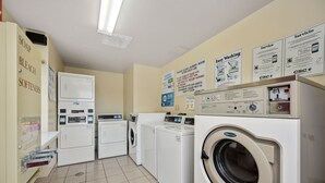 A laundry facility with multiple washing machines, a dryer, and a wall-mounted dispenser for soap, bleach, and softeners. - Affordable Suites Hickory/Conover (Conover)