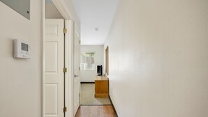 A narrow hallway with wooden flooring, white walls, and a door leading to a room with a window and a small wooden shelf. - Affordable Suites Hickory/Conover (Conover)