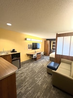 Quarto de hotel pequeno com cozinha compacta, televisão de tela plana, sofá e uma cama.