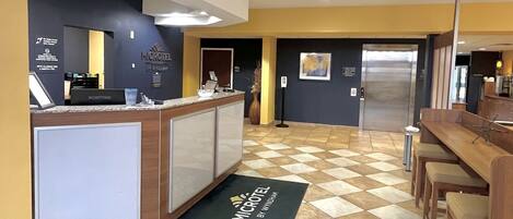 Un vestíbulo de hotel con mostrador de recepción, máquina expendedora y zona de estar con mostrador de entrada.