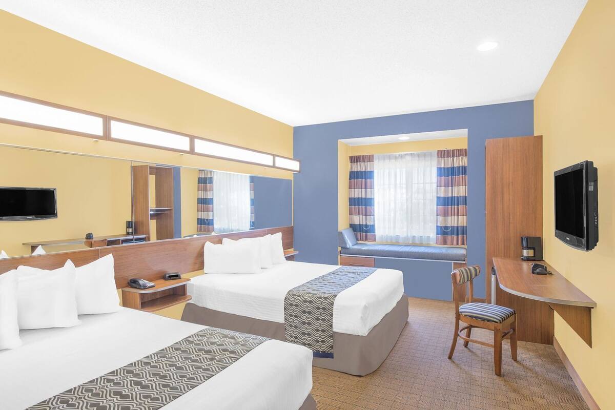 A hotel room with two beds, a desk, a chair, a TV, and a window with curtains.