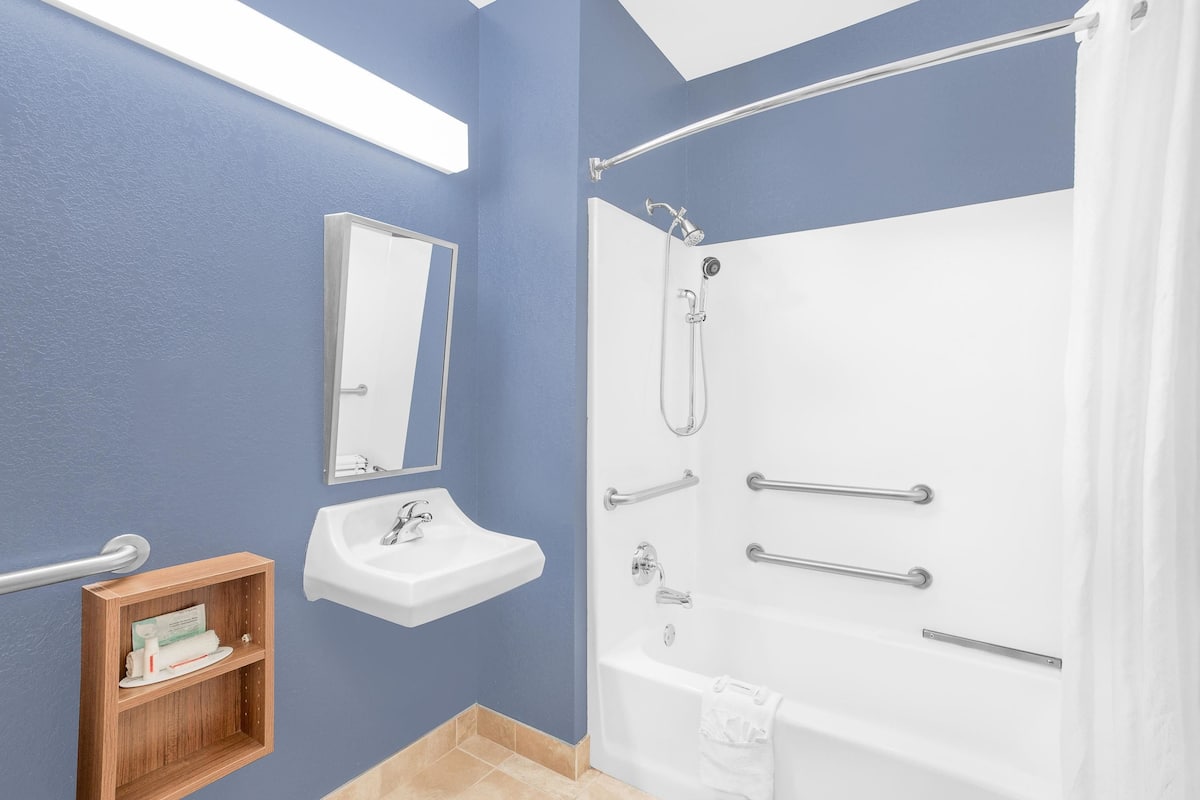A bathroom with a white bathtub, a sink, a mirror, and a wooden medicine cabinet.