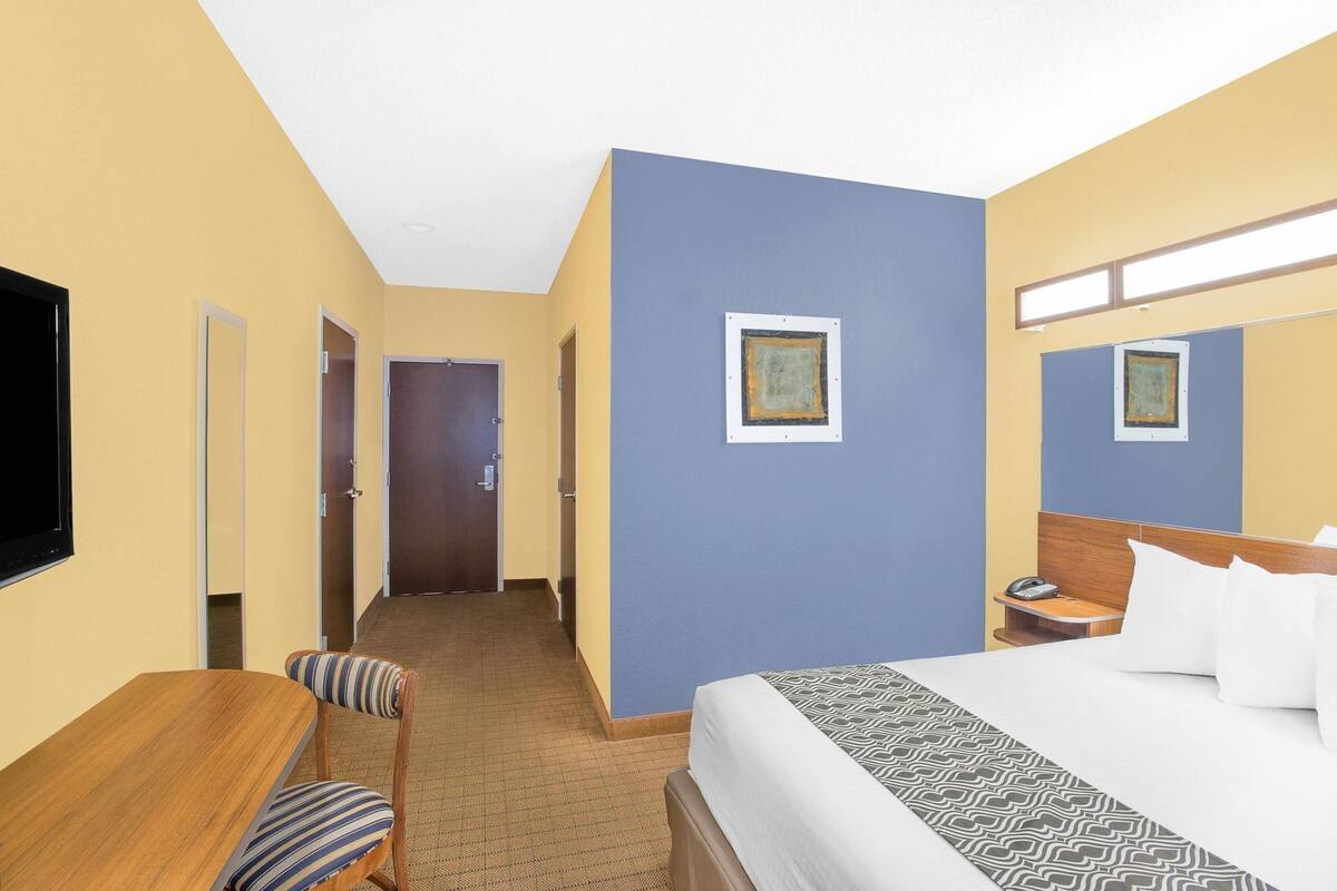 A hotel room with a bed, a desk, a chair, a television, and a door.