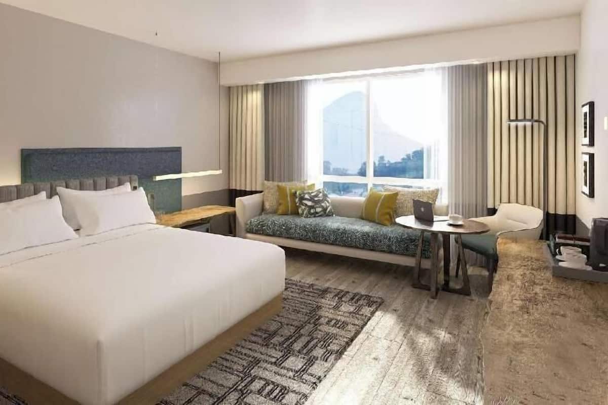 Une chambre d’hôtel avec un grand lit, un canapé, une petite table et une fenêtre avec des rideaux.