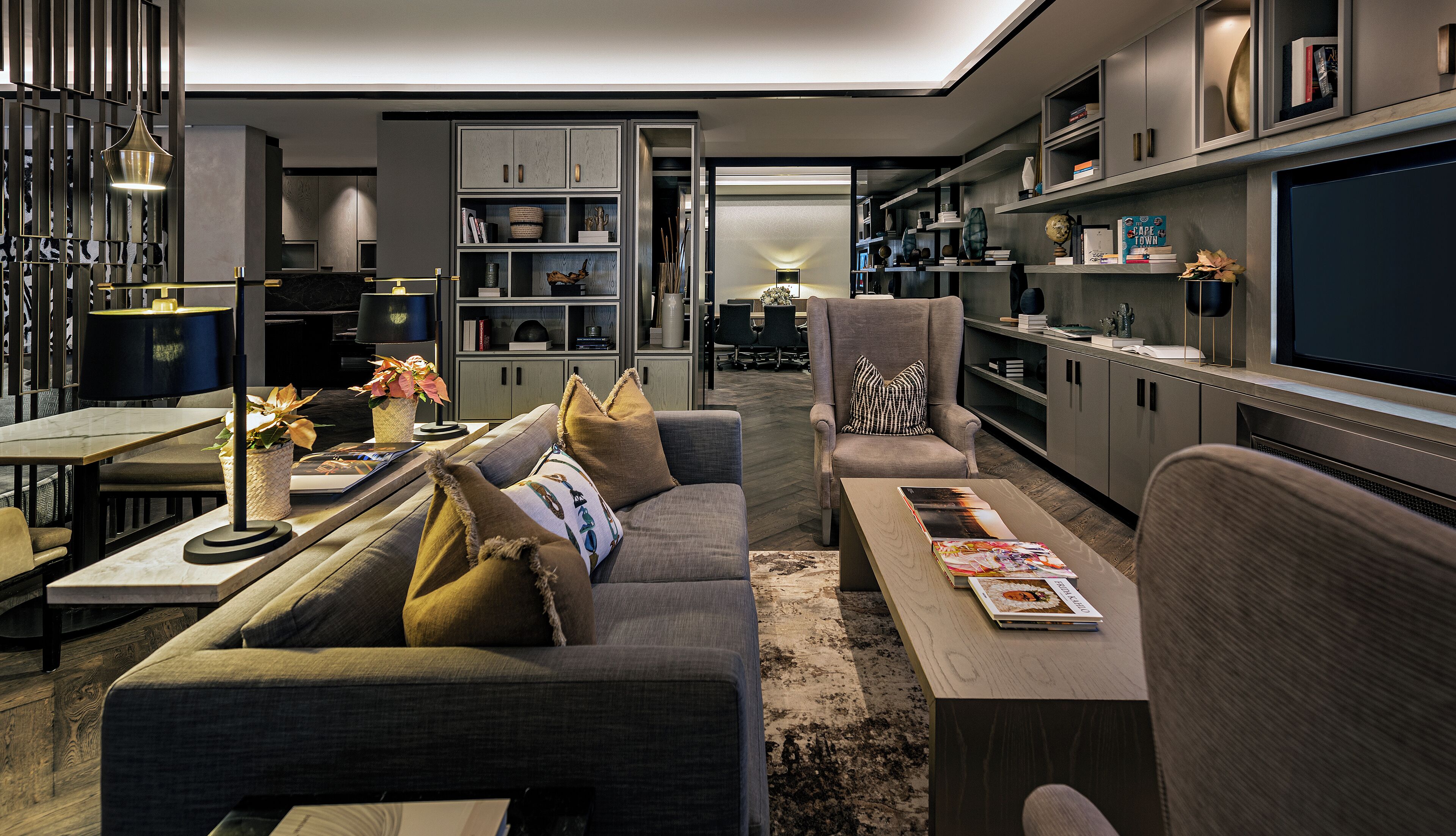 A modern living room with a sofa, coffee table, and a TV. There are bookshelves and a dining area with a table and chairs.