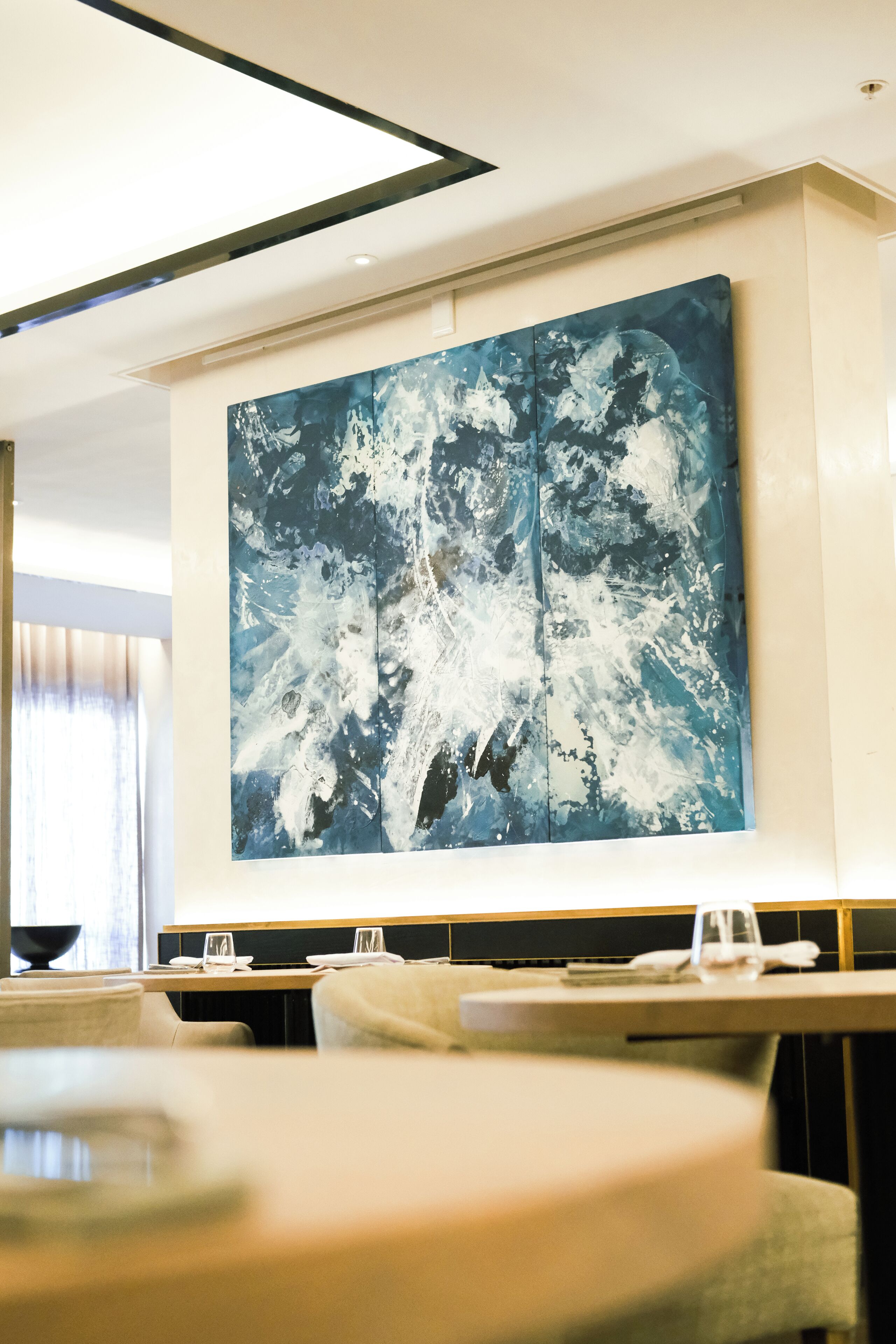 Un espace de restauration moderne, agrémenté d’un grand tableau abstrait au mur, de tables disposées avec soin et d’un design contemporain au niveau du plafond.