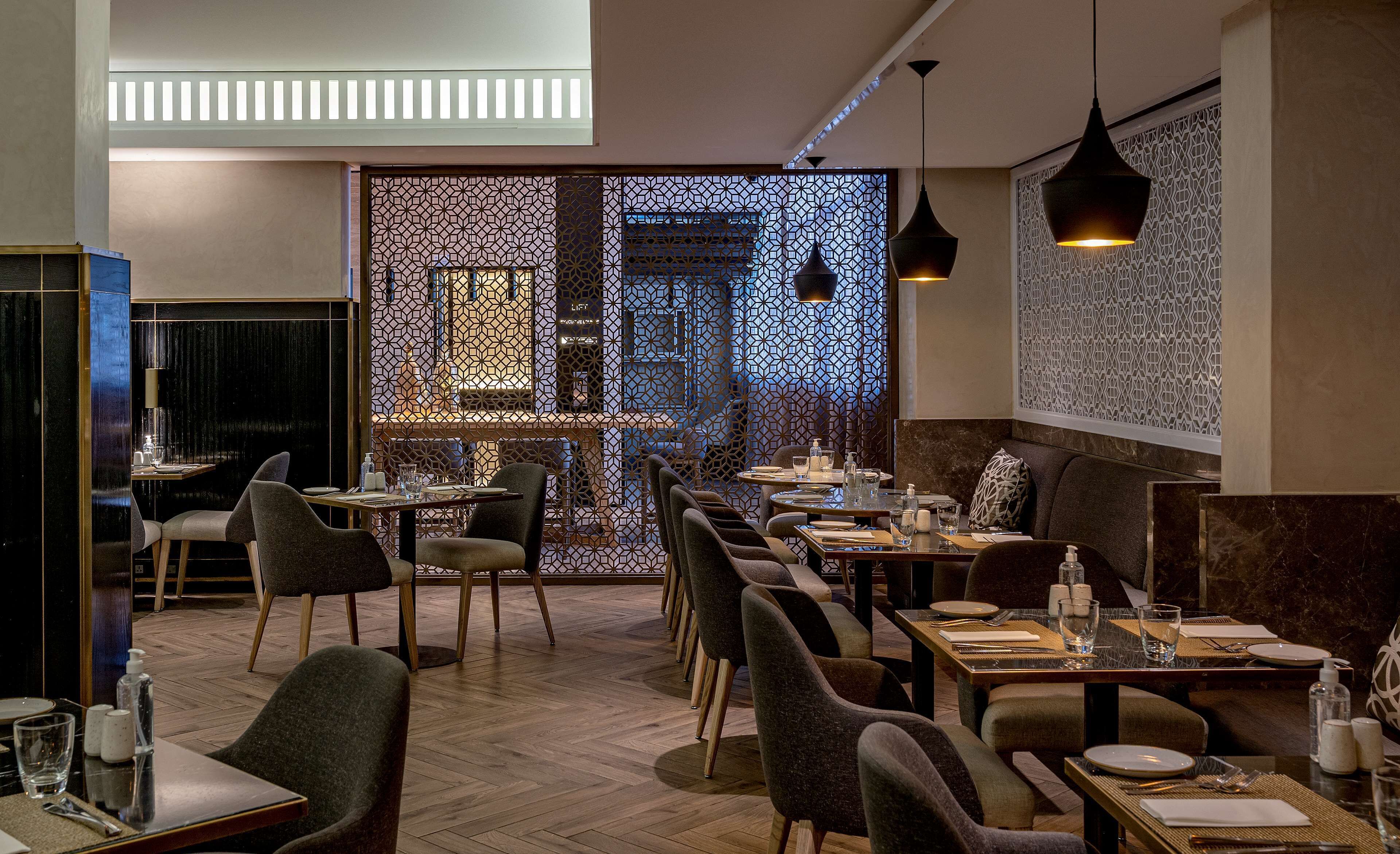 Un interior de restaurante con piso de madera, sillas modernas y mesas listas para comer.