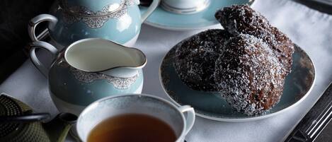 A tray with a teapot, two cups, a saucer, and a pastry on a marble surface.