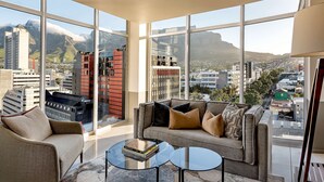 A modern living room with a sofa and a coffee table, large windows offering a cityscape view. - Hyatt Regency Cape Town (Cape Town)