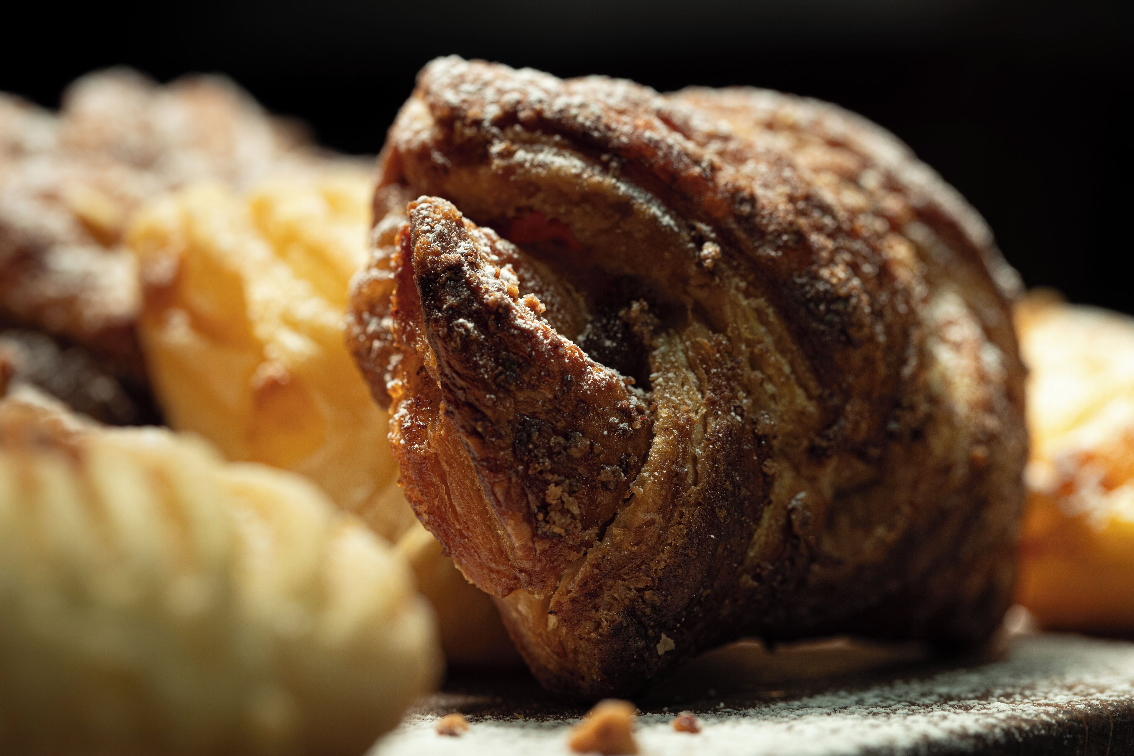 A close-up of a baked pastry with a golden-brown crust, possibly a croissant or similar bread, with a dusting of flour on top.