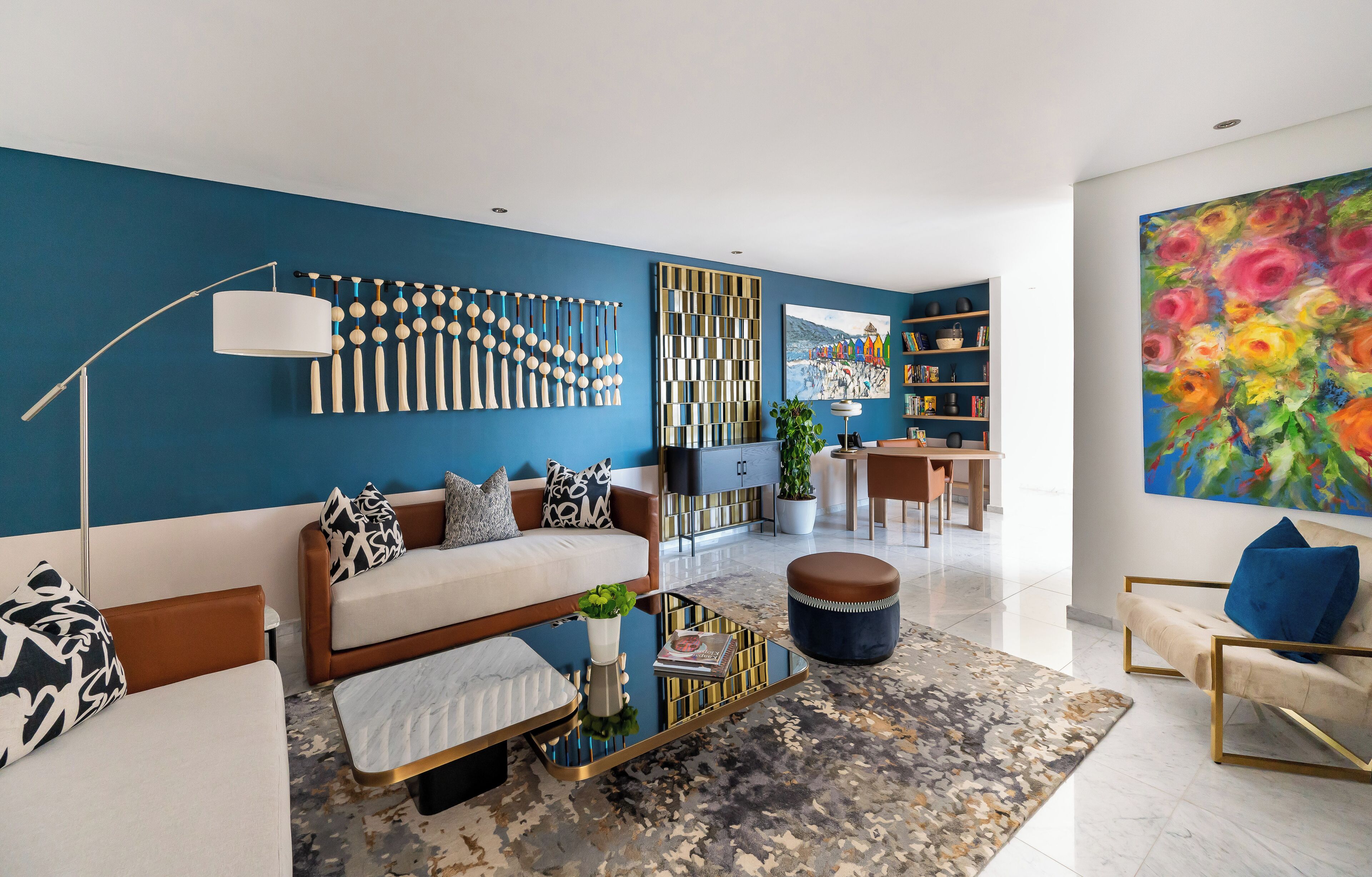 Ein modernes Wohnzimmer mit blauer Akzentwand, einer Sofagarnitur, einem Couchtisch, einer Stehlampe und einem großen Gemälde.