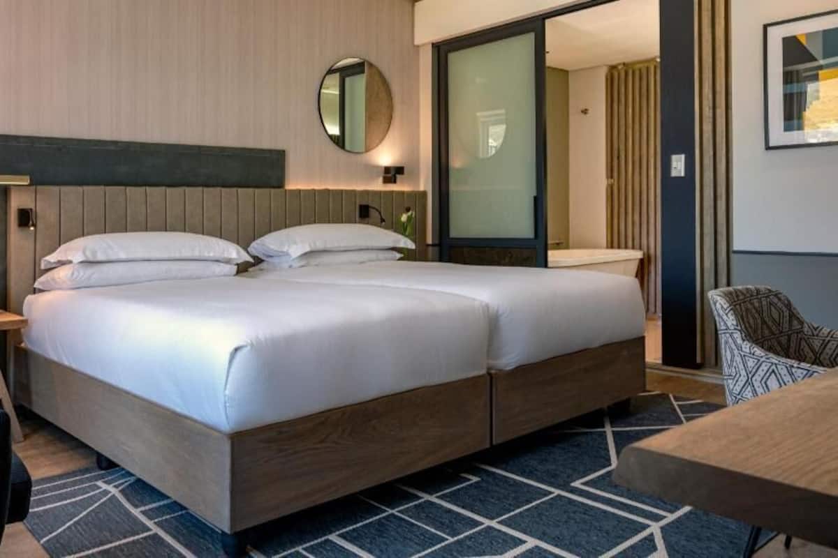 A modern hotel room with a large bed, bedside tables, a desk, and a chair.