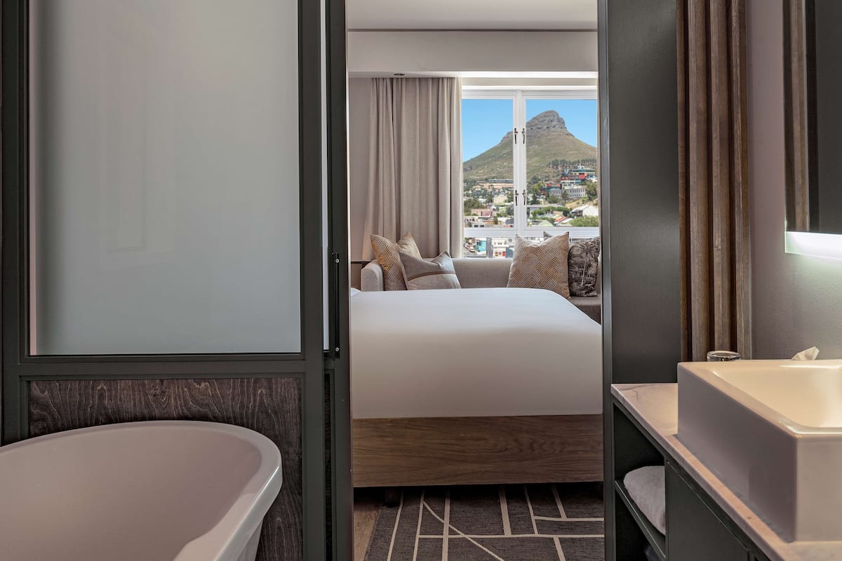 Une chambre d’hôtel avec un grand lit, une baignoire, un lavabo et une vue sur la montagne et la ville.