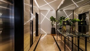 A modern hallway with a mirrored wall, a black elevator, and a long table with plants and lamps. - Hyatt Regency Cape Town (Cape Town)