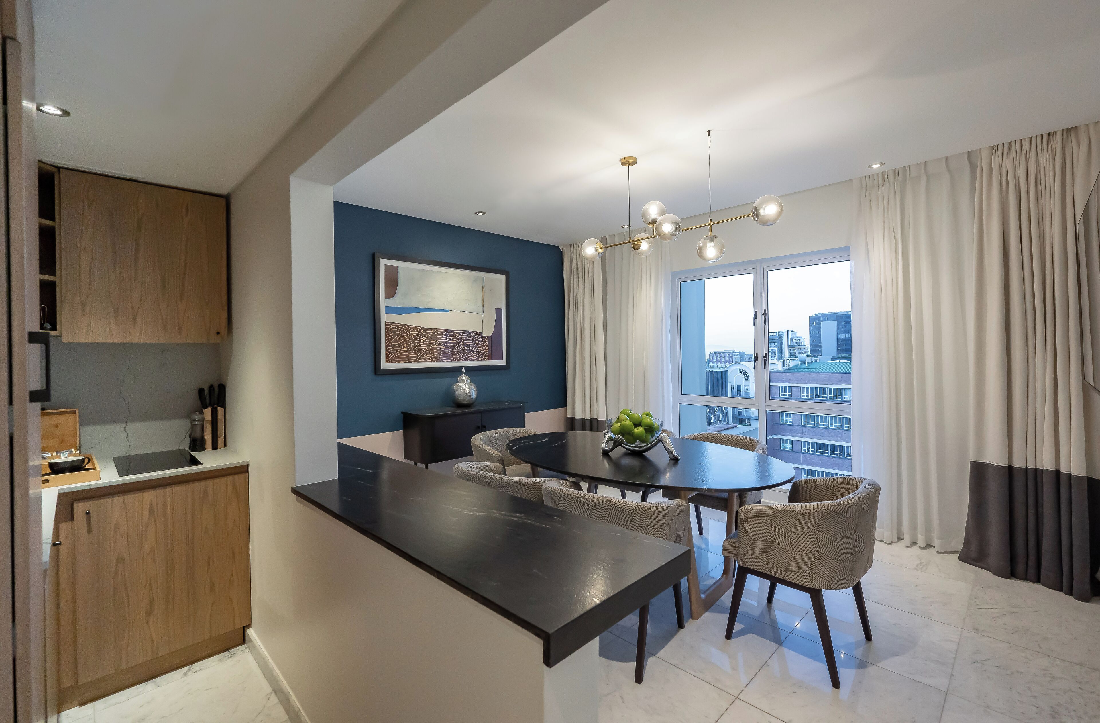 Una cocina moderna con una isla central, comedor con sillas y un amplio ventanal con cortinas.