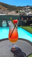 A cocktail with a strawberry garnish and a black straw, placed on a table by a pool.