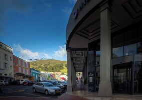 A street view with parked cars, a building with a modern facade, and a clear blue sky.