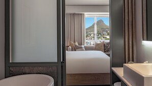 A hotel room with a large bed, a bathtub, and a view of a mountain and town. - Hyatt Regency Cape Town (Cape Town)
