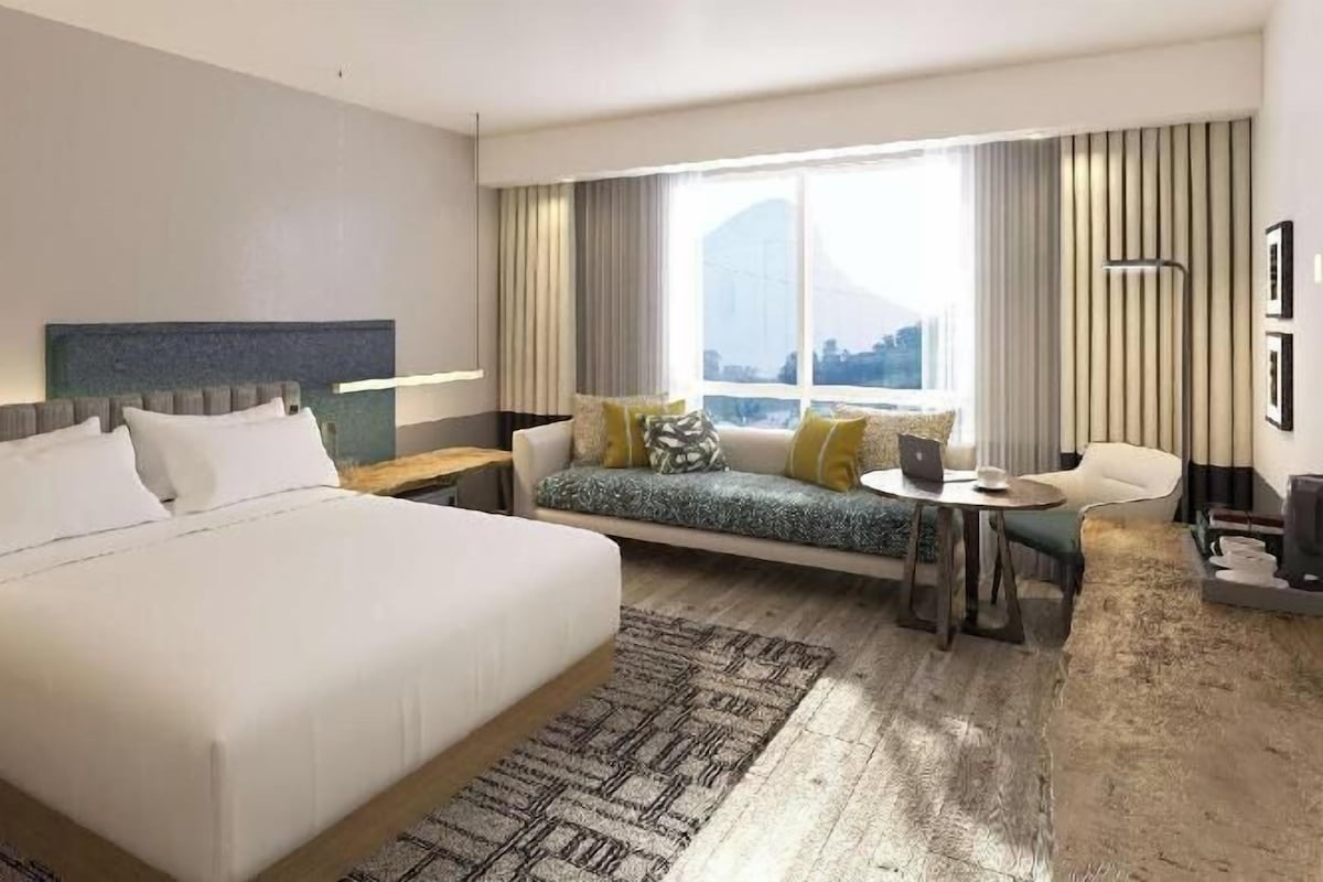 A hotel room with a large bed, a sofa, a small table, and a window with curtains.