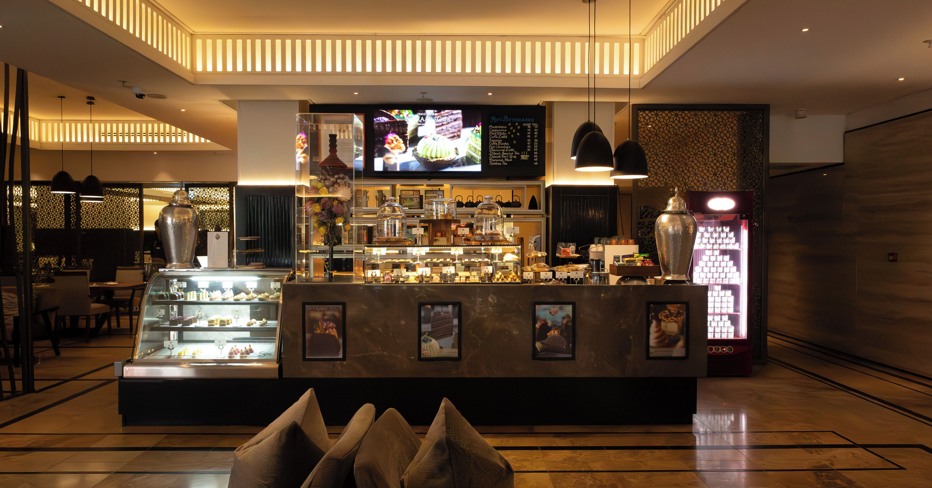Mostrador de postres con un panel de menú, luces colgantes y una gran pantalla de televisión.