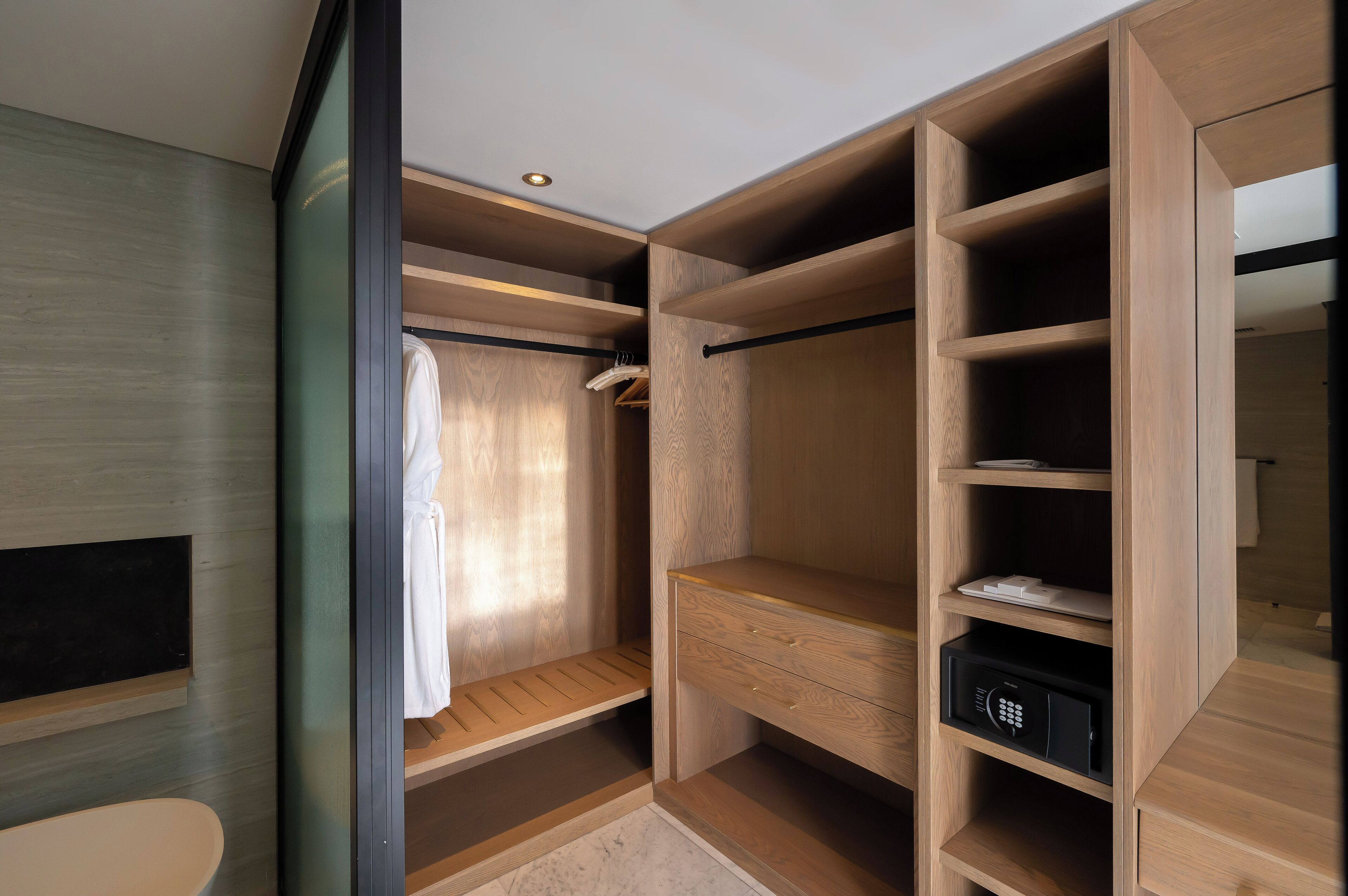 Un vestidor con estanterías de madera, una barra para colgar ropa y una caja fuerte empotrada.