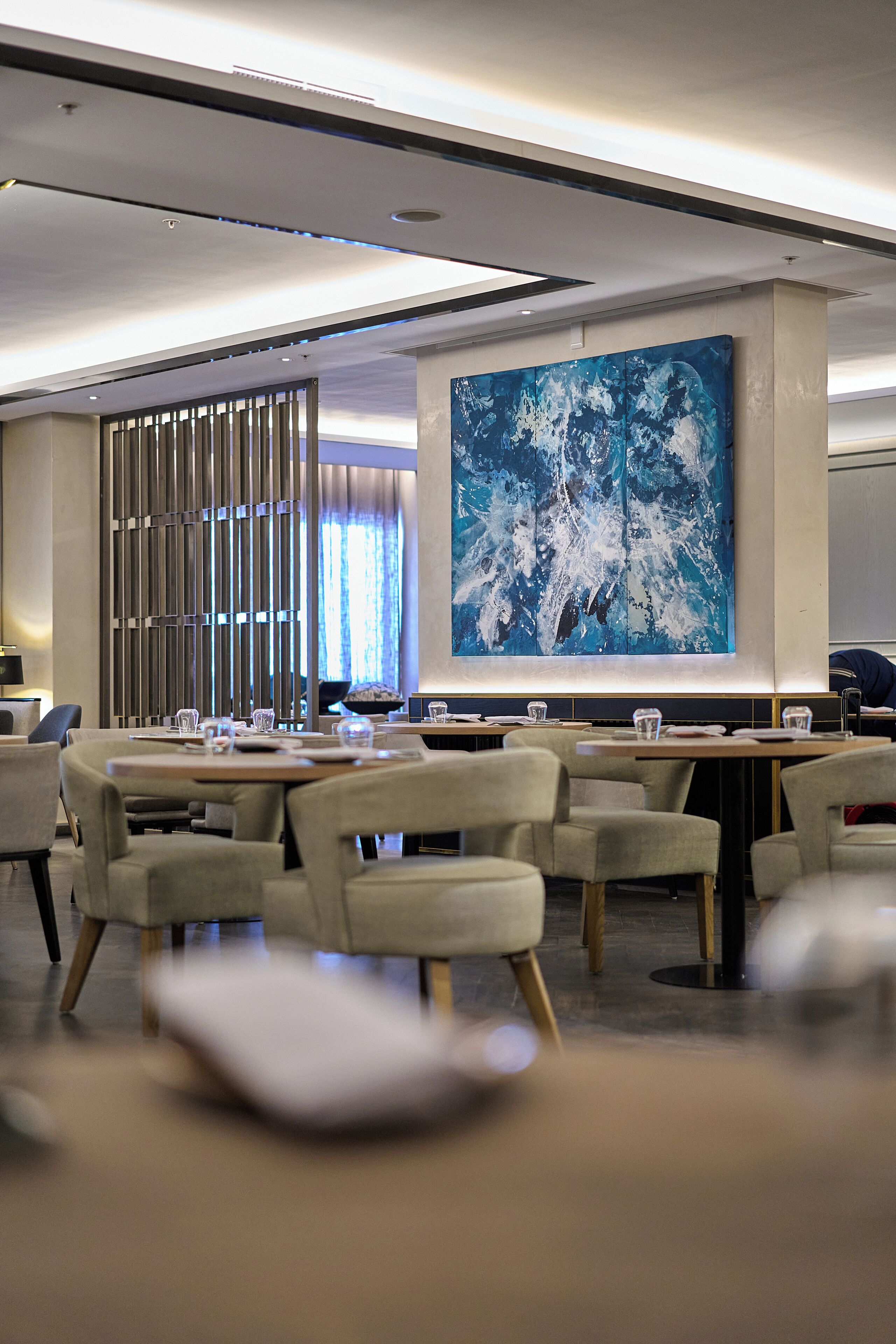 A modern dining area with tables and chairs, a large abstract painting on the wall, and a partition with vertical slats.
