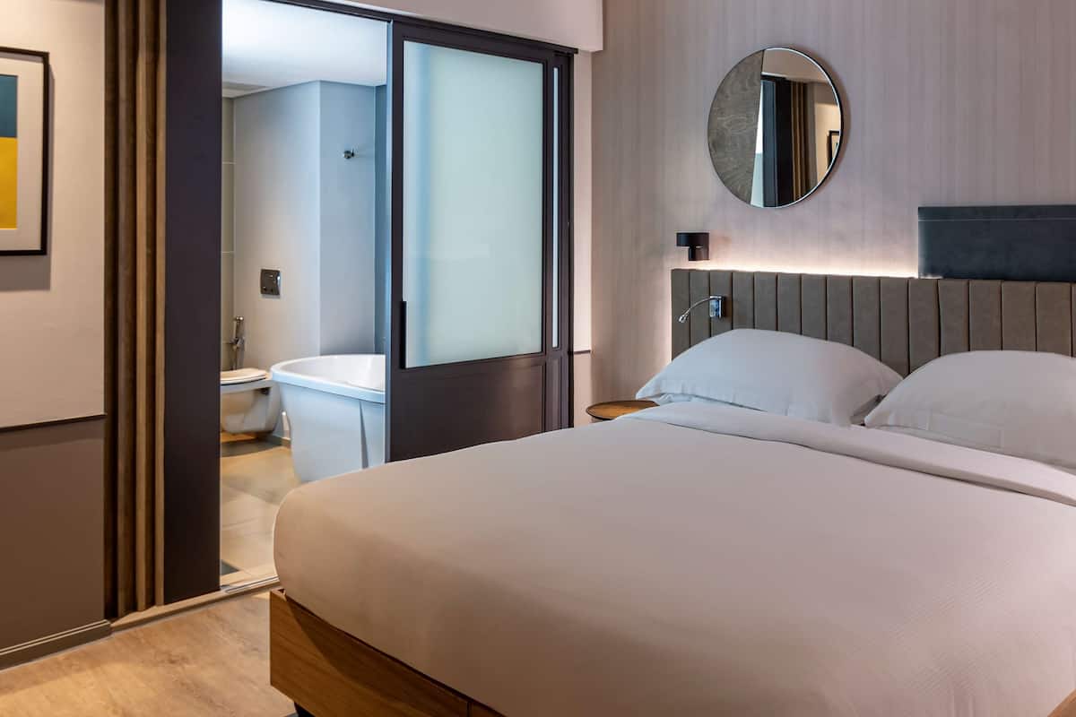 Une chambre d’hôtel moderne avec un grand lit, un miroir rond et une vue sur la salle de bain.