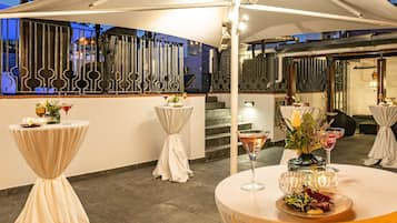 Un área de comedor al aire libre con mesas redondas, manteles blancos y centros de mesa con velas.