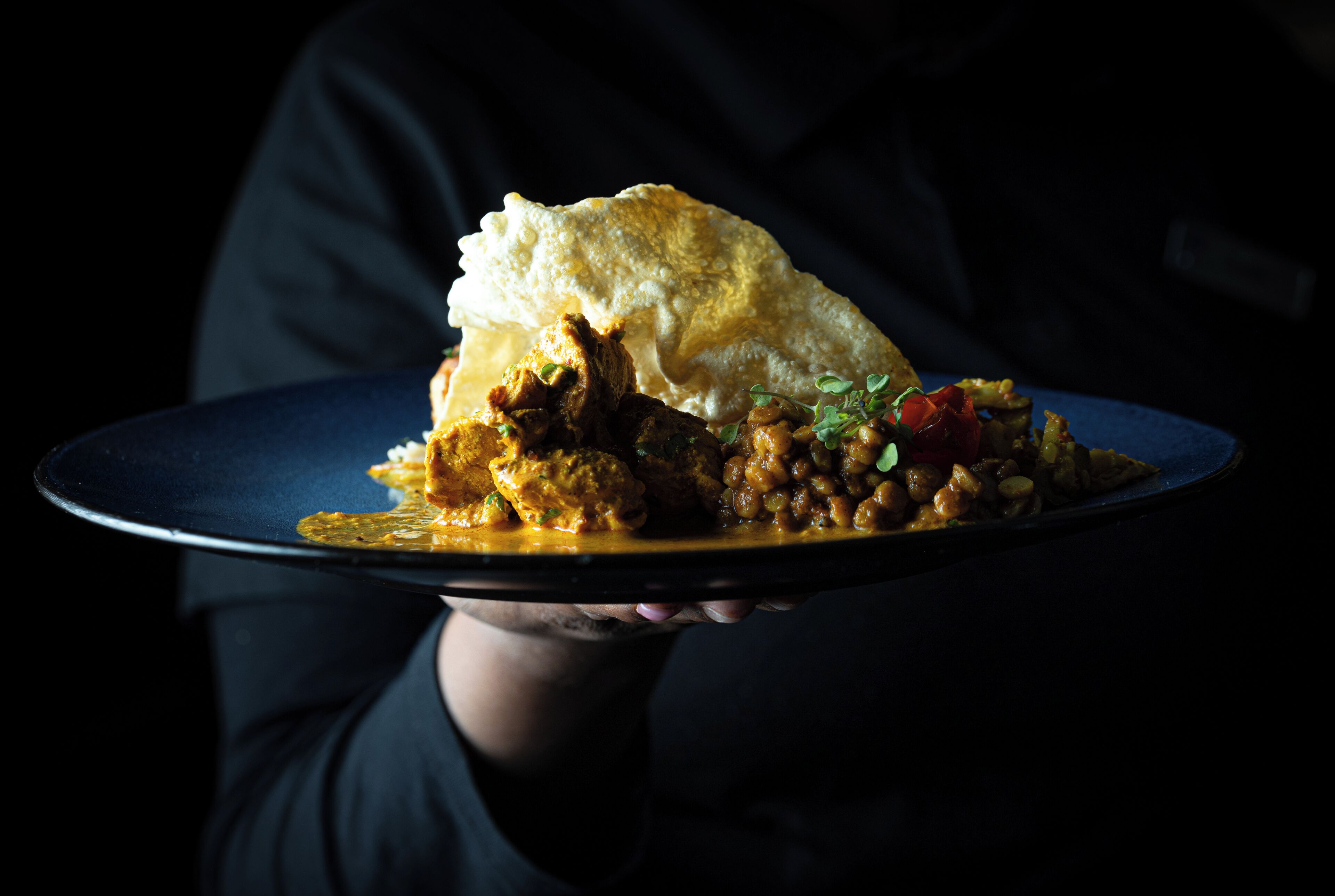 A person holding a plate with a dish that includes a piece of bread and a meat-based stew with beans and vegetables.