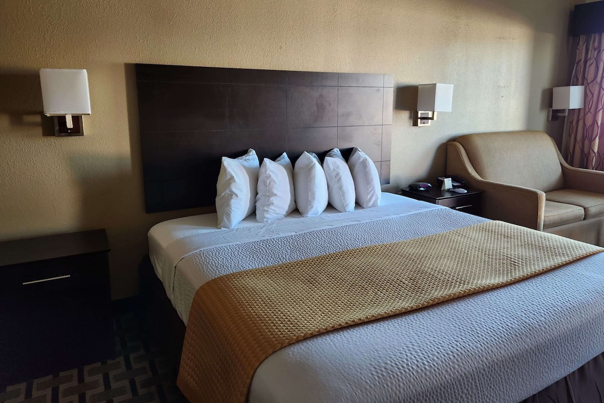 Hotellihuone, jossa on suuri sänky, pääty, kaksi yöpöytää, tuoli ja seinään kiinnitetyt lamput.