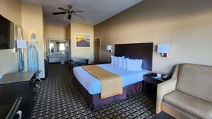 A hotel room with a bed, a desk, a chair, a sofa, a ceiling fan, and a large window. - Days Inn by Wyndham Baytown East (Baytown)