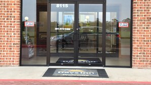 A Day Inn entrance with a glass door, a brick wall, and a welcome mat. - Days Inn by Wyndham Baytown East (Baytown)