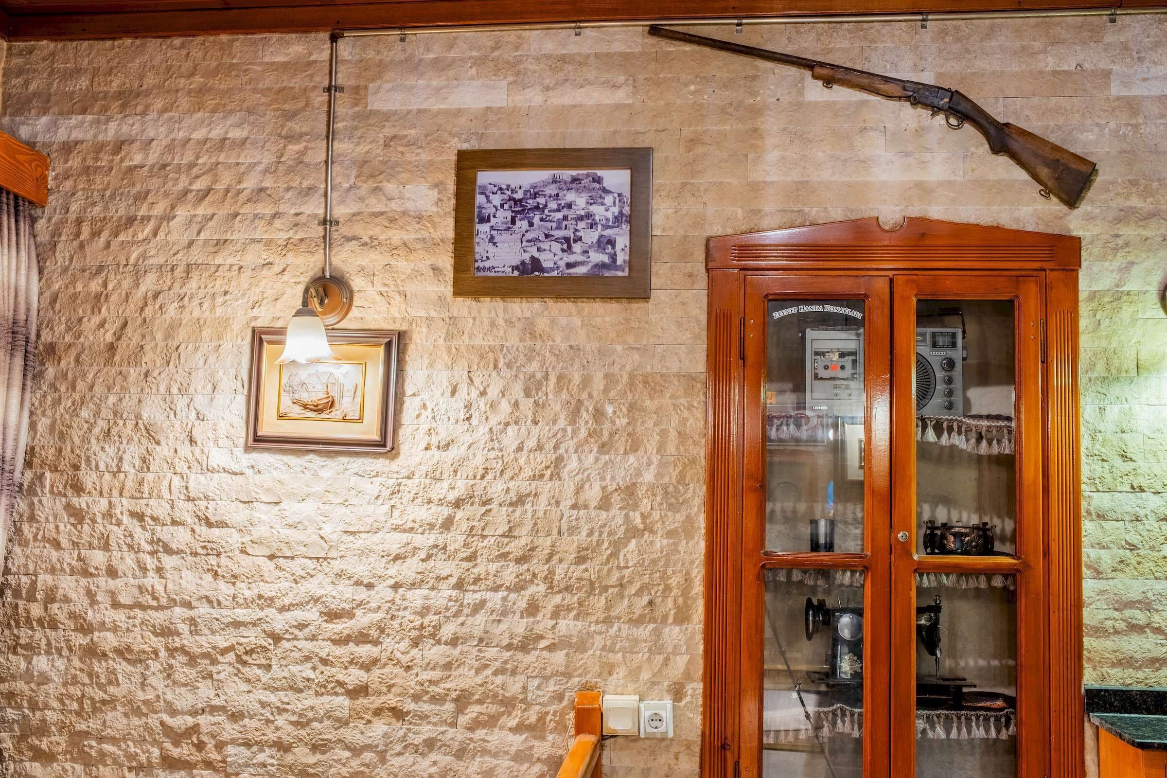 A room with a stone wall, a wooden cabinet with glass doors, a framed picture, and a hanging light fixture.
