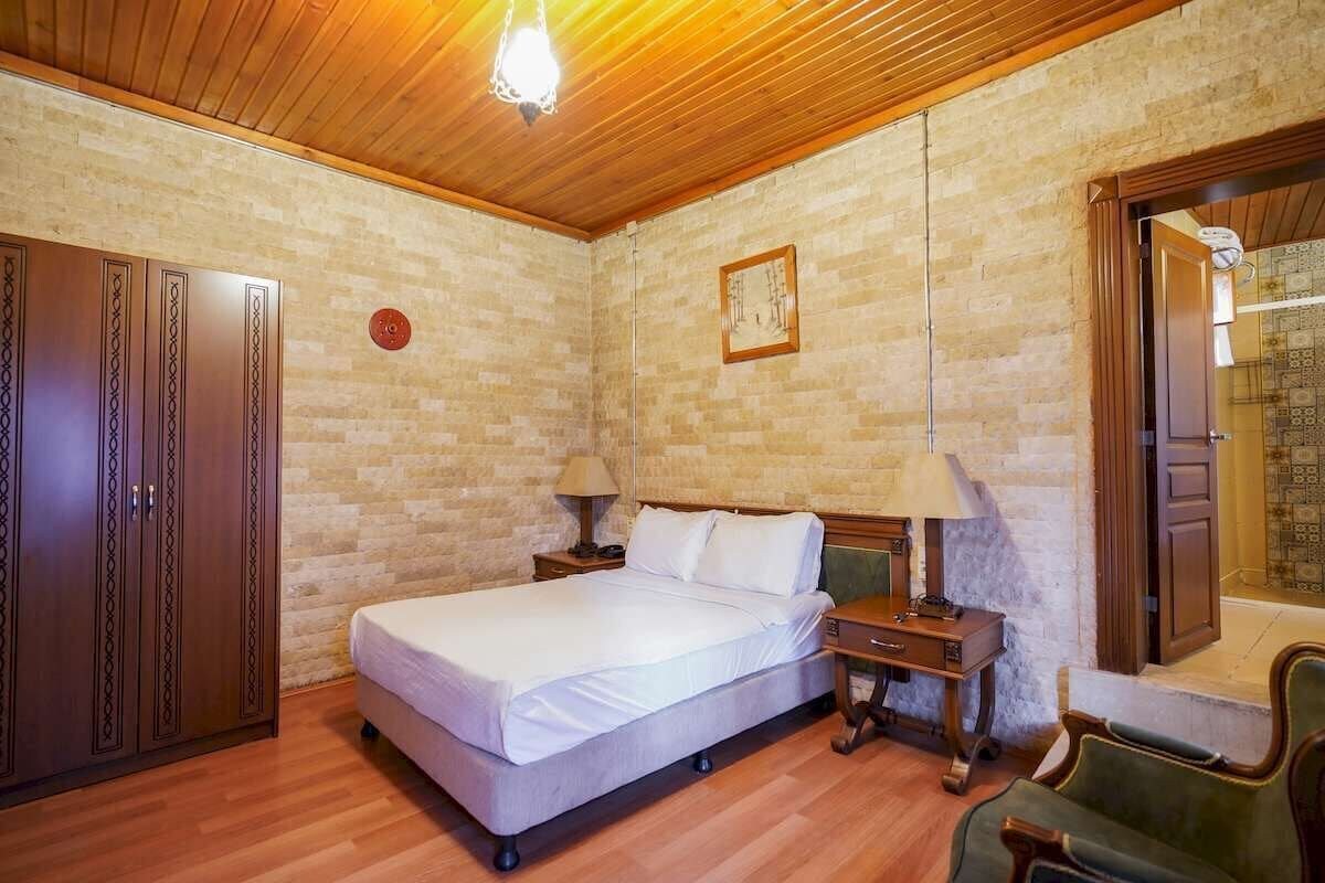 A bedroom with a wooden ceiling, a bed with white bedding, a nightstand, a lamp, a wardrobe, and a chair.