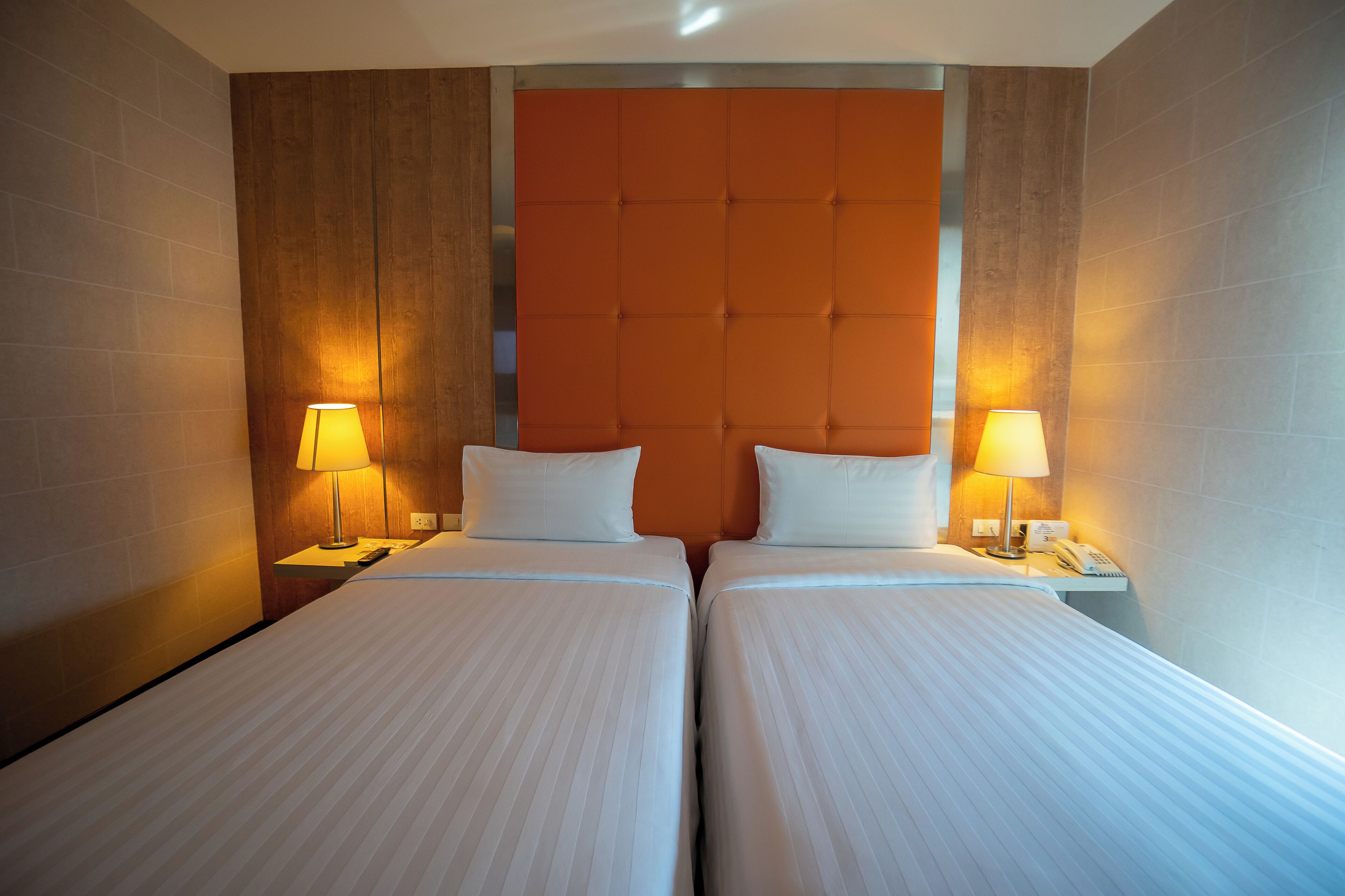 A hotel room with two beds, a wooden headboard, and bedside lamps.