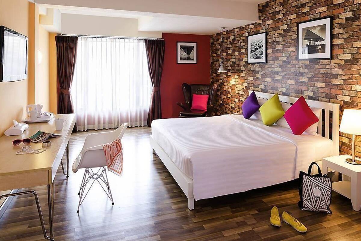 A hotel room with a bed, desk, chair, and a brick wall.